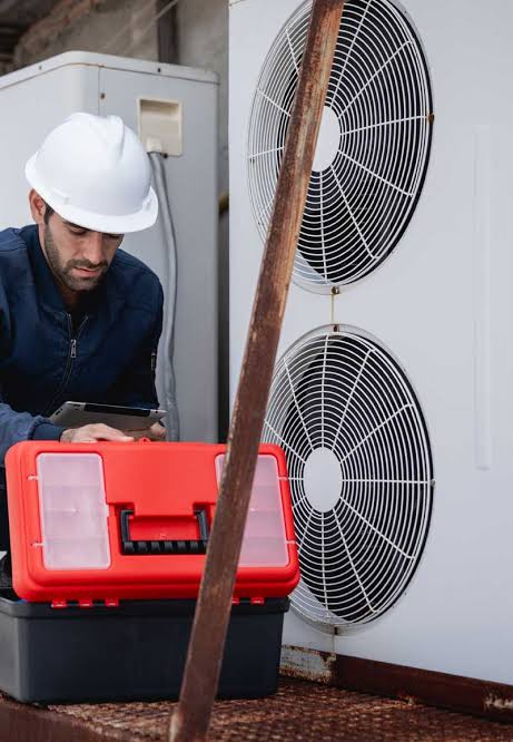 HVAC technician wearing a hard hat checking equipment beside a twin-fan outdoor air conditioning system